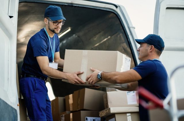 Young couriers cooperating while unloading packages from deliver Delivery men loading carboard boxes in a van while getting ready for the shipment.